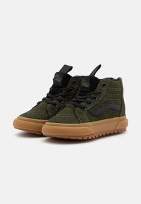 Zapatillas altas de ante verde con acentos negros, suela de goma y agarre texturizado. Presenta costuras visibles y una etiqueta en el cuello.