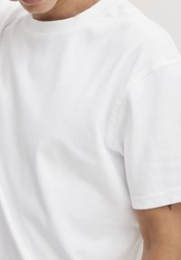 Witte katoenen T-shirt met een ronde hals, korte mouwen en zichtbare stiksels. Zachte textuur met een lichte glans.