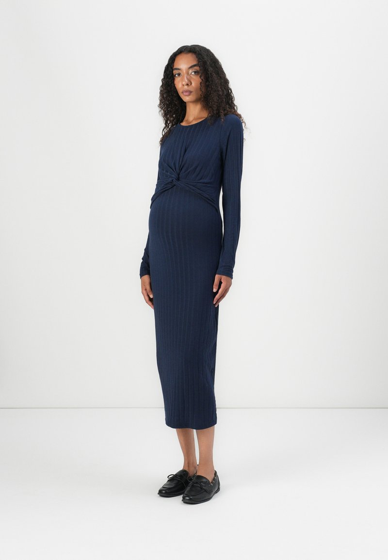 Navy ribbat midi-klänning med långa ärmar och en vriden framsida. Tyget är slätt och stretchigt, vilket förstärker den figursydda siluetten.