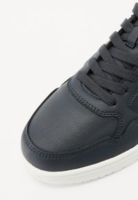 Marineblå lærersneakers med teksturert overdel, flate snører, hvit mellomsåle og kontrasterende sømmer langs sømmene. Rund tådesign.