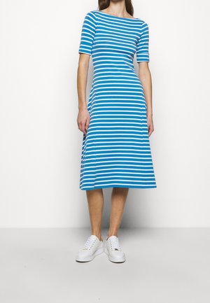 Robe mi-longue à rayures bleues et blanches avec un corsage ajusté et une jupe évasée. Matière en coton, manches courtes, associée à des baskets blanches.