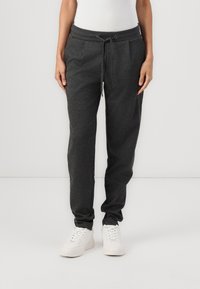 Tmavě šedé tepláky vyrobené z měkké tkaniny, s bočními kapsami, elastickým pasem se šňůrkou a zužujícími se nohavicemi.