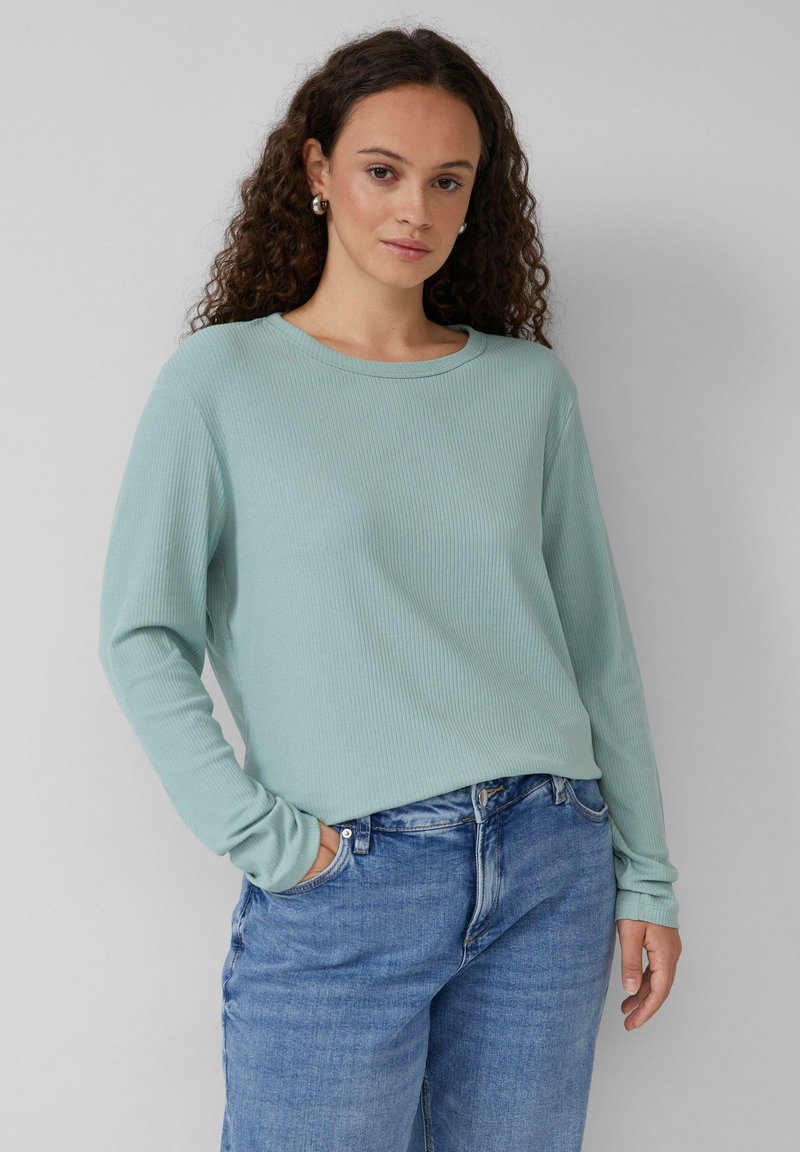 Hellmintgrünes, geripptes Langarmoberteil mit Rundhalsausschnitt, kombiniert mit hellblauen, tapered Jeans. Der Stoff hat eine weiche Textur.