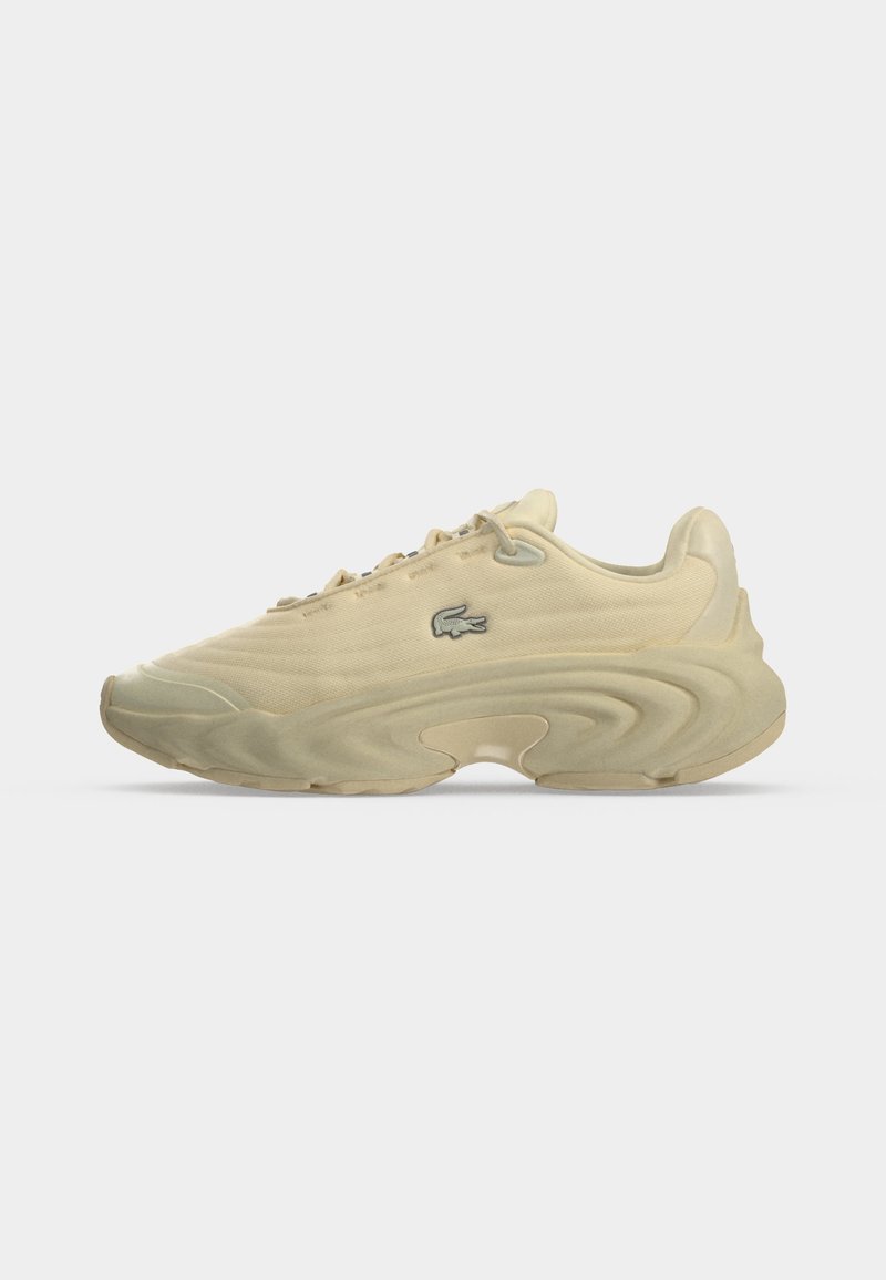 Sneaker beige low-top con suola spessa scolpita, chiusura frontale con lacci e piccolo logo verde di coccodrillo sul lato su sfondo uniforme.