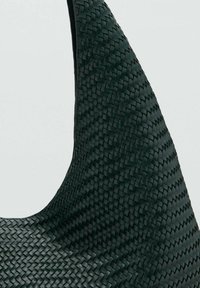 Sac à main tissé vert présentant une forme incurvée distinctive et une finition texturée, mettant en évidence un motif en forme de panier à travers le matériau.