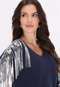 Marineblauer Pullover mit V-Ausschnitt, ausgestattet mit silbernen Paillettenfransen an den Schultern, strukturiertem Stoff und einer lockeren Passform.