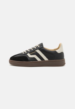 Black and cream athletic shoes with suede and leather materials, featuring a textured brown sole and gold logo accents.