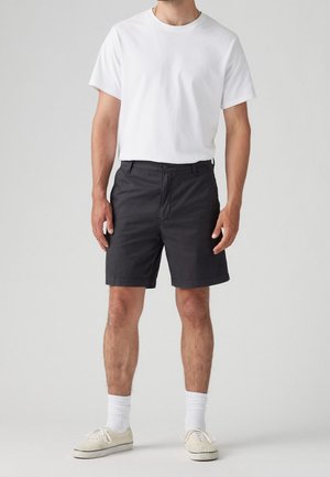 Schwarze Baumwollshorts mit geradem Schnitt, vorderen Taschen und klassischem Bund, kombiniert mit einem schlichten weißen T-Shirt und hellen Sneakers.