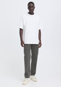 Tricou alb cu mâneci scurte, blugi gri cu croială dreaptă și adidași bej. Textură netedă, asemănătoare bumbacului; croială lejeră; design minimalist.