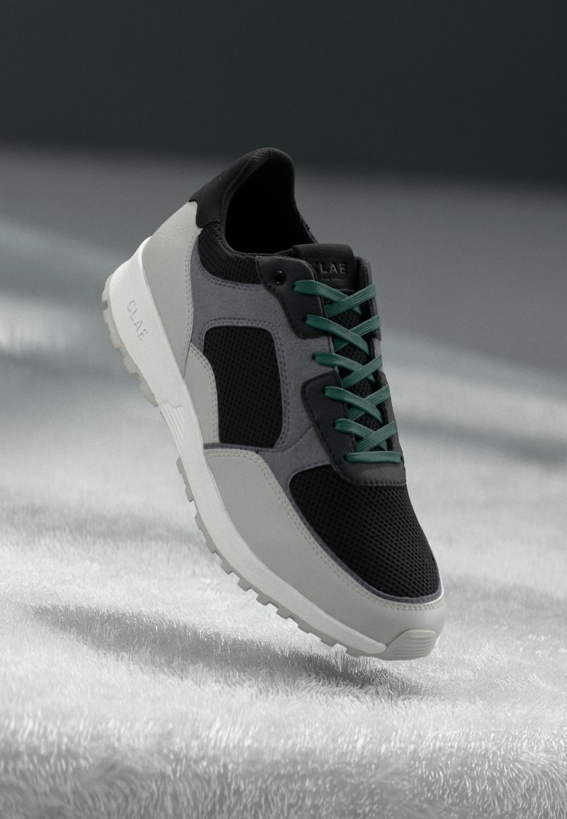 Black and gray sneaker with mesh panels, teal laces, and a white sole. Features a smooth texture and rounded toe design.