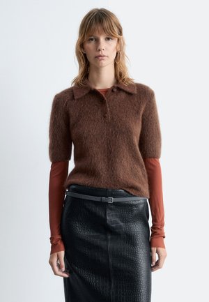 Brown, fuzzy short-sleeve sweater with a collar and buttons, layered over a fitted rust long-sleeve shirt, paired with a black, textured leather skirt.
