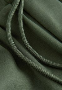 Detailný záber tmavozelenej látky s dvoma zladenými tkanými šnúrkami ležiacimi na jej povrchu.