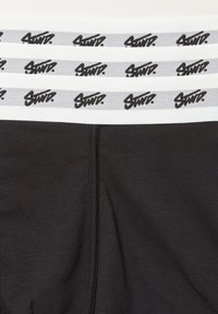 Čierne boxerky s bielym elastickým pásom zdobené opakovanými čiernymi potlačami loga "Stüssy". Hladká textúra a priliehavý strih.