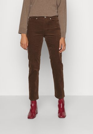 Bruna kordbyxor med slim fit, med detaljer av metallknappar och nitar, kombinerat med blanka röda klackstövlar.