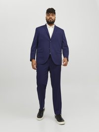 Navy blue suit with two-button blazer and flat-front trousers. Worn over a white shirt, paired with black sneakers. Smooth fabric texture.