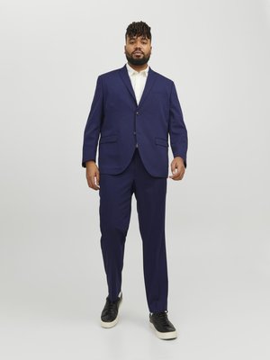 Navy blue suit with two-button blazer and flat-front trousers. Worn over a white shirt, paired with black sneakers. Smooth fabric texture.