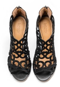 Paire de sandales à talons ouvertes noires avec des motifs découpés complexes et des semelles intérieures couleur fauve, vues de dessus.