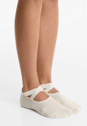 Chaussettes de ballet beige clair avec des sangles croisées, fabriquées en matériau doux et extensible, présentant une texture lisse et un ajustement serré autour du pied.