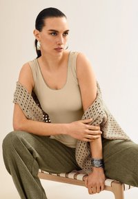Beige geripptes Tanktop mit rundem Halsausschnitt, kombiniert mit olivgrünen gemusterten Weitbein-Hosen und einem hellbraunen gestrickten Schal.