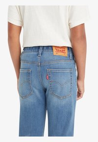 Světle modré denimové džíny s viditelnou značkovou cedulkou, zadní kapsy s vyšívaným vzorem a pohodlným střihem.