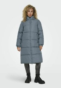 Manteau d'hiver long gris en duvet avec un col haut, doté d'une fermeture éclair sur le devant et de poches latérales. Le design comprend des sections matelassées et des poignets élastiques.