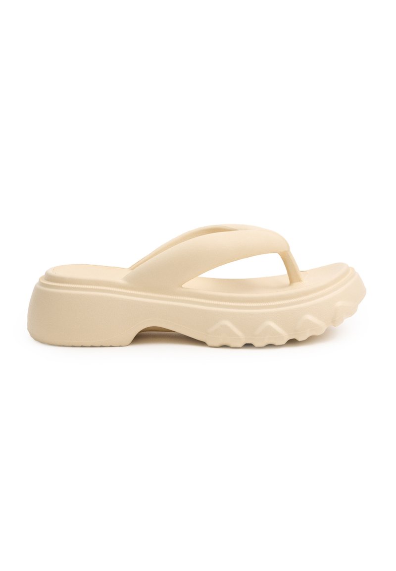 Chancla de goma beige con suela gruesa, diseño de punta abierta y fondo texturizado que presenta pequeñas estrías y detalles a lo largo de los lados.