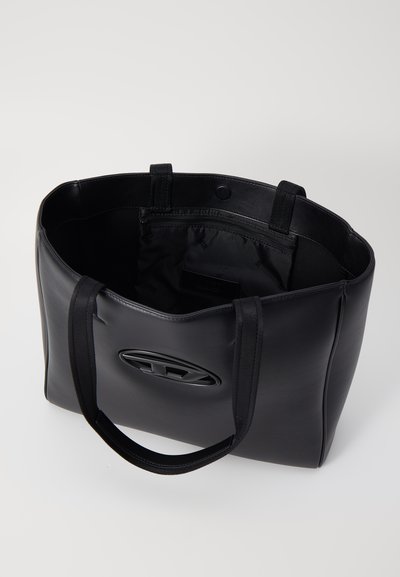 Sac fourre-tout en cuir noir avec une texture lisse, une forme arrondie et des poignées doubles. Présente un logo sur le devant et un compartiment zippé à l'intérieur.