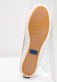 Semelle de basket Keds avec une surface en caoutchouc texturé de couleur beige et un logo Keds bleu. Bordure blanche et design à bords arrondis.