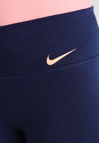 Närbild av marinblå sporttights med rosa Nike swoosh-logotyp vid midjan, i kombination med en rosa topp.