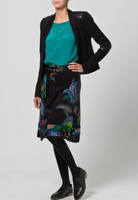 Czarna spódnica w kolorowe kwiatowe wzory, zestawiona z turkusową bluzką i czarną marynarką z skórzanymi akcentami. Czarny rajstopy i buty dopełniają wygląd.