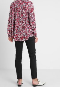 Flowy floral blouse in red with white and blue flowers, paired with black fitted pants and white slip-on shoes, with decorative accents.