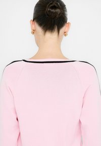 Helles rosa Sweatshirt mit rundem Ausschnitt, ausgestattet mit schwarzen Akzenten an den Schultern und am Ausschnitt, sowie einem weichen, strukturierten Strick. 