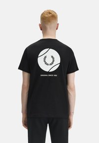 T-shirt in cotone nero con una grafica circolare bianca che presenta una corona di alloro e il testo "ORIGINAL SINCE 1952" sul retro. Maniche corte.