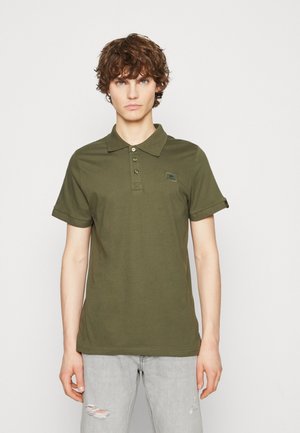 Tricou polo verde măsliniu cu guler, trei nasturi și un patch cu logo pe piept. Mânici scurte cu tiv rulat, fabricat din bumbac moale.