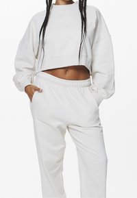 Sudadera blanca recortada con mangas largas y un cuello alto, combinada con joggers blancos a juego con cintura elástica y bolsillos.