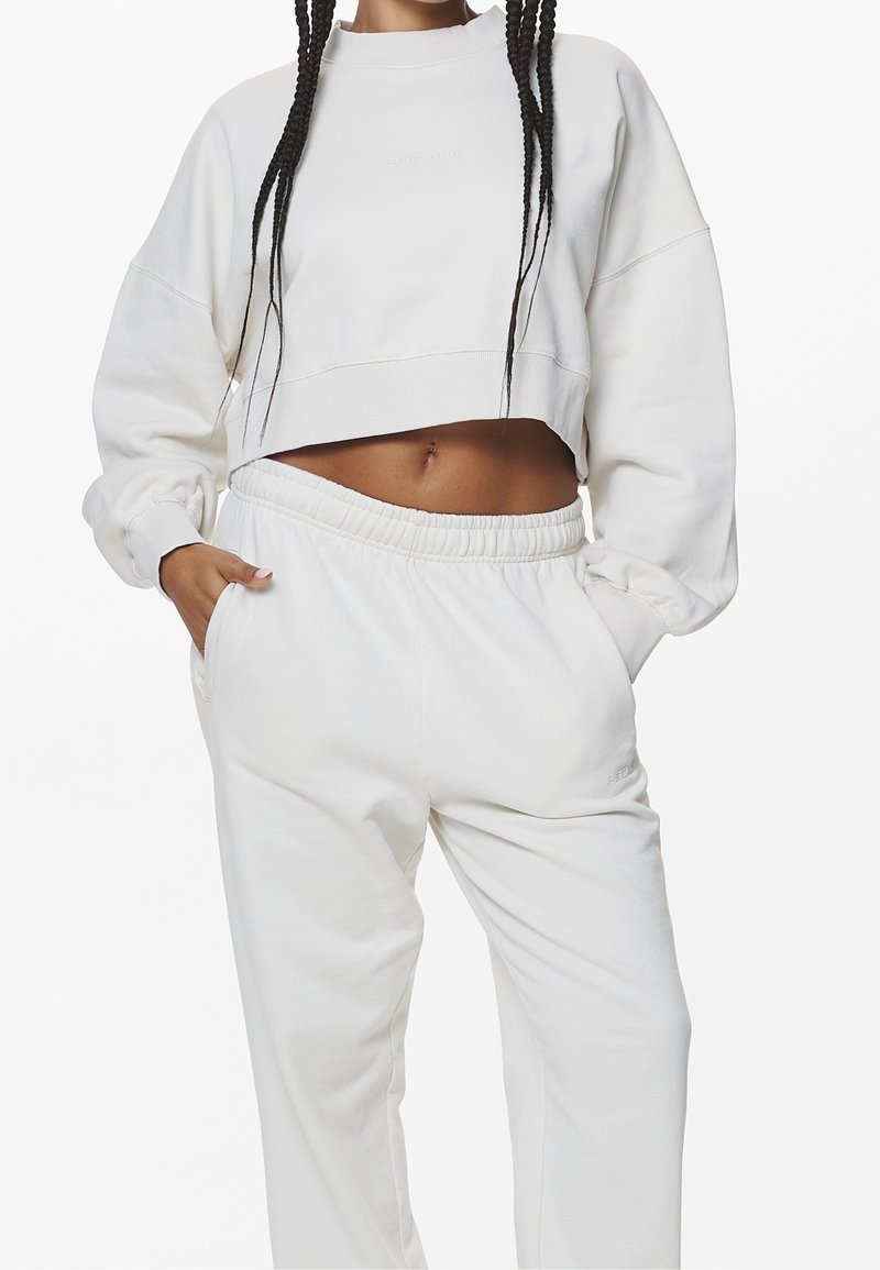 Sudadera blanca recortada con mangas largas y un cuello alto, combinada con joggers blancos a juego con cintura elástica y bolsillos.