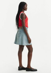 Débardeur en crochet rouge, jupe en denim bleu clair en forme de A et chaussures noires à profile bas. La jupe possède une poche arrière et un ourlet effiloché.