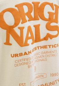 Bílý bavlněný tričko s velkým oranžovým blokovým textem. Design obsahuje "ORIGINALS" a "URBAN AESTHETICS" v tučné typografii.
