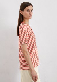 Gestreiftes T-Shirt in Orange und Weiß, kurze Ärmel, V-Ausschnitt-Design, leichtes Material, lässige Passform, kombiniert mit hellbeigen Hosen.