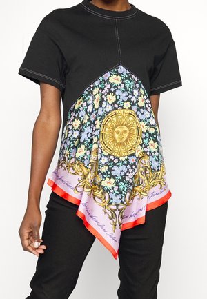 Black short-sleeve top with floral patterned scarf panel featuring a gold sun emblem and red trim, worn with black pants.