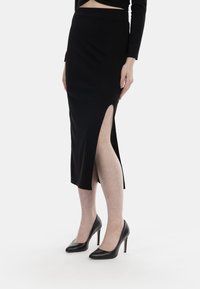Schwarzer Midirock mit hohem Schlitz, aus geripptem Stoff gefertigt. Kombiniert mit schwarzen High Heels, die ein elegantes Design zeigen.