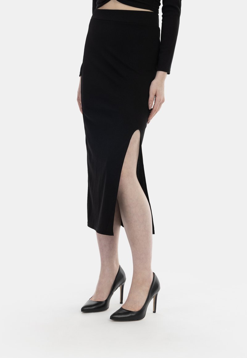 Schwarzer Midirock mit hohem Schlitz, aus geripptem Stoff gefertigt. Kombiniert mit schwarzen High Heels, die ein elegantes Design zeigen.