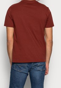 Kortærmet, bordeaux t-shirt lavet af bomuld, med en klassisk rund halsudskæring og en afslappet pasform. Bæres med blå denim jeans.