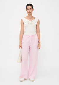 Top bianco con colletto a cappuccio, pantaloni di lino rosa larghi con cordino in vita, trama liscia. Look casual completato con sneakers bianche e una borsa piccola.