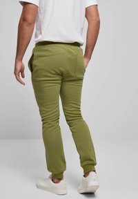 Grüne Baumwoll-Jogginghosen mit zulaufenden Beinen, elastischem Bund und Seitentaschen, kombiniert mit weißen Sneakers und einem schlichten weißen T-Shirt.