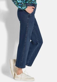 Dunkelblaue Jeans aus Denim mit geradem Bein, ausgestattet mit Seitentaschen und dezenten Nähten, kombiniert mit weißen Sneakern.
