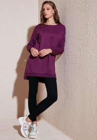 Felpa lunga viola abbinata a leggings neri e sneakers bianche. La parte superiore presenta una vestibilità comoda e un colletto rotondo.