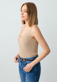 Beige geribbelde bodysuit met een V-hals en dunne bandjes, gecombineerd met hoge, blauwe spijkerbroeken en een bruine riem. Gladde textuur, aansluitend ontwerp.