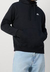 Svart sweatshirt med huva, med en känguruficka och en liten vit logotyp på bröstet. Material i bomullsblandning, avslappnad passform.