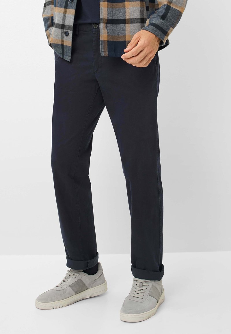 Navy chinos met een slim fit, gemaakt van soepel stof. Gecombineerd met lichtgrijze suède sneakers en een geruiten flanellen shirt in gedempte kleuren.
